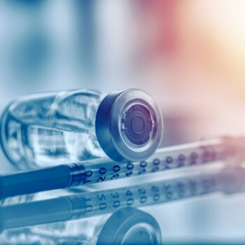 A vial laid on its side on-top of a syringe.