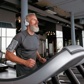 An older man with headphones running on a treadmill