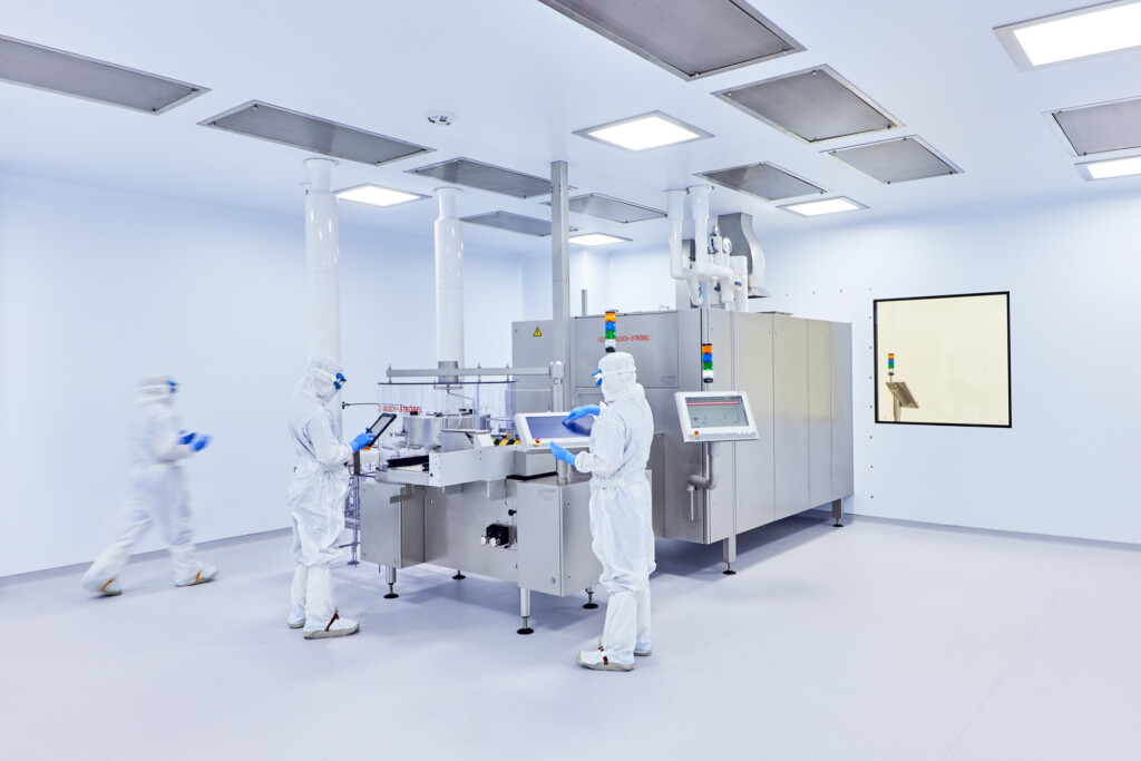 Three workers in white clean suits working at a large machine