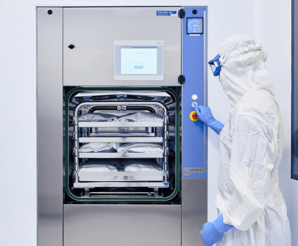 A worker in a white clean suit and goggles pressing a button on steel machine.