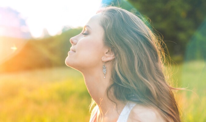 A woman closing her eyes facing the sun outside