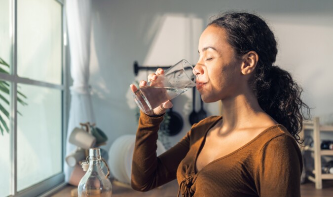 A woman drinking a glass of water with the sun shining on her.