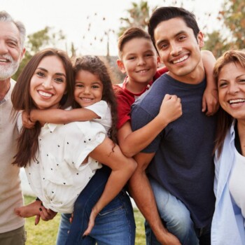A family of six happy people in a field looking at the camera.