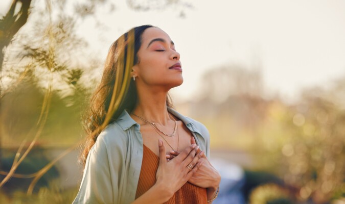 A woman holding her hands to her chest breathing deeply while outside