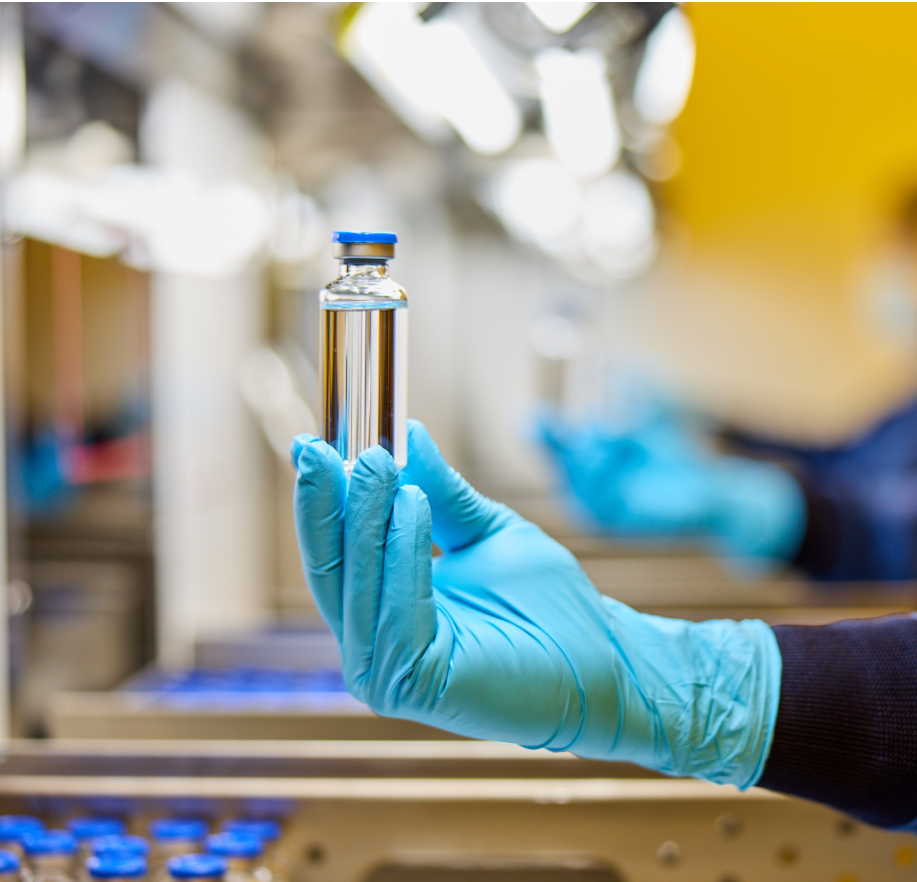 A gloved hand holding a vial of clear liquid
