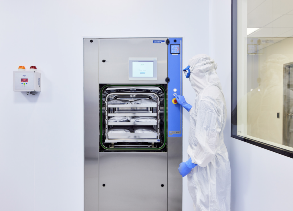 A worker in a white clean suit pressing a button on a steel machine.