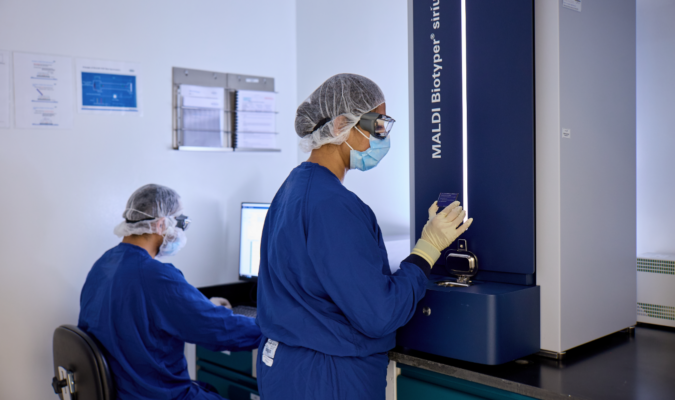 A worker in a blue clean suit and a hair net holding something near a machine.