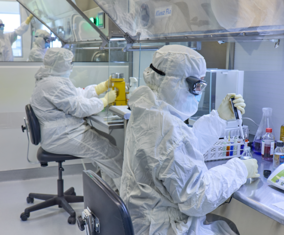 Workers in white clean suits with goggles measuring stuff while sitting down.