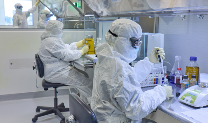 Workers in white clean suits with goggles measuring stuff while sitting down.