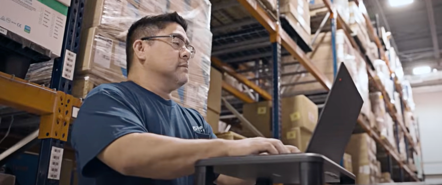 A man in a warehouse looking at a computer.