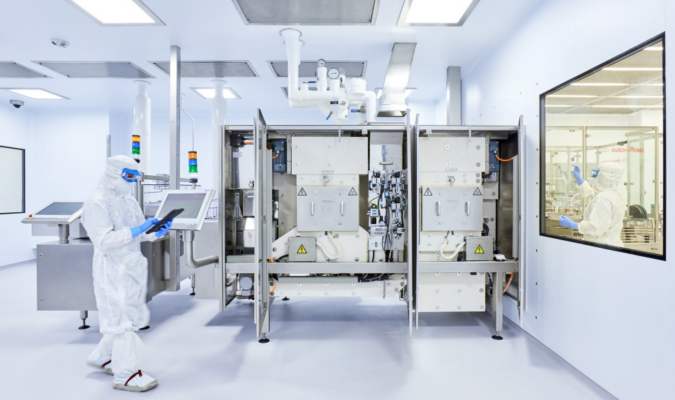 A worker in white clean suits using a tablet near a machine