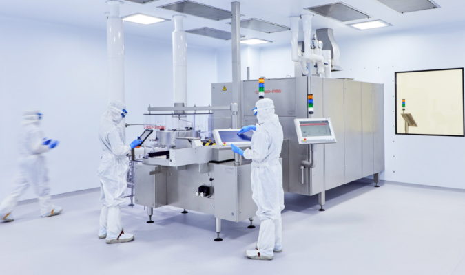Three workers in white clean suits using a machine