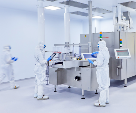 Three workers in white clean suits using a machine