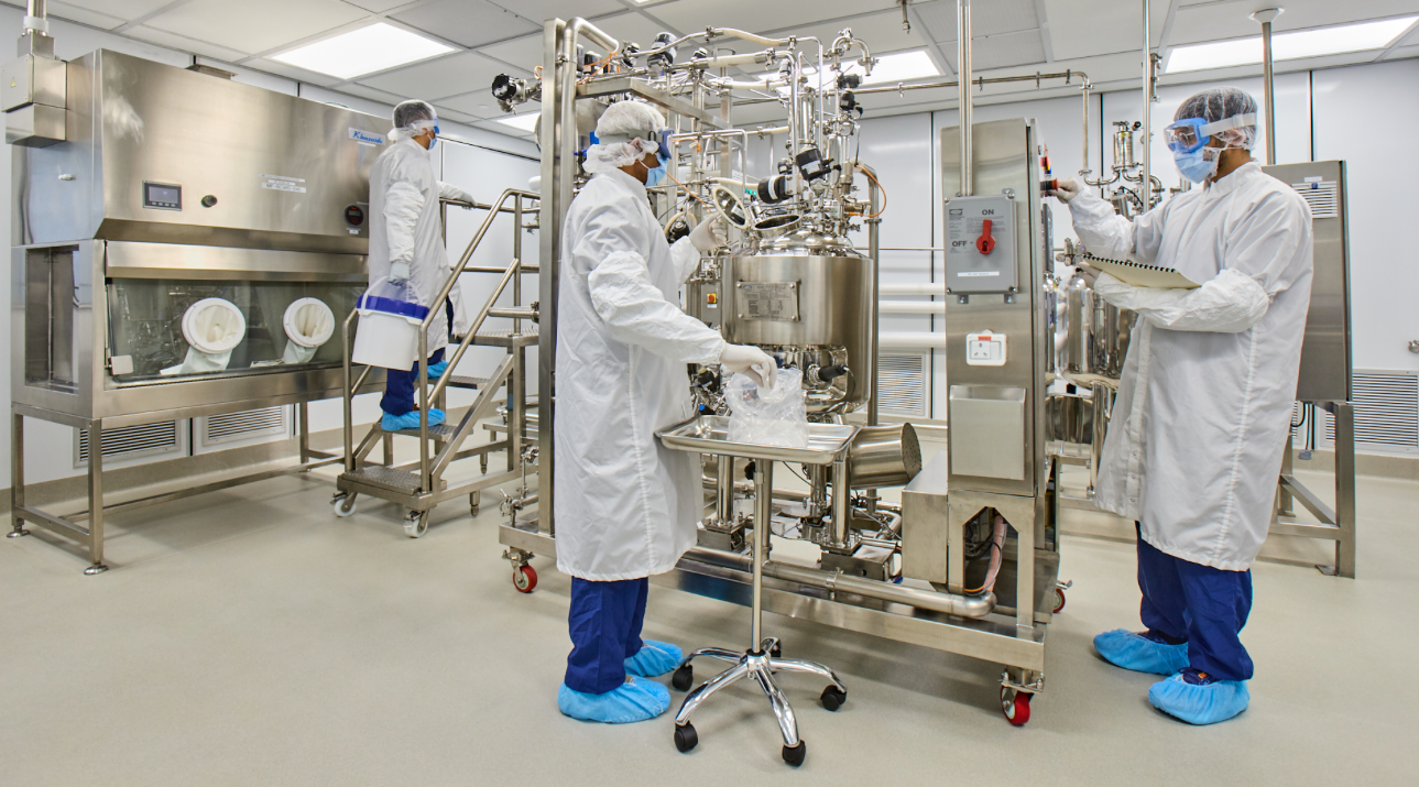 Two workers in white clean suits using a machine