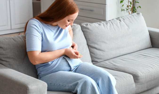 woman sitting on couch giving self an injection