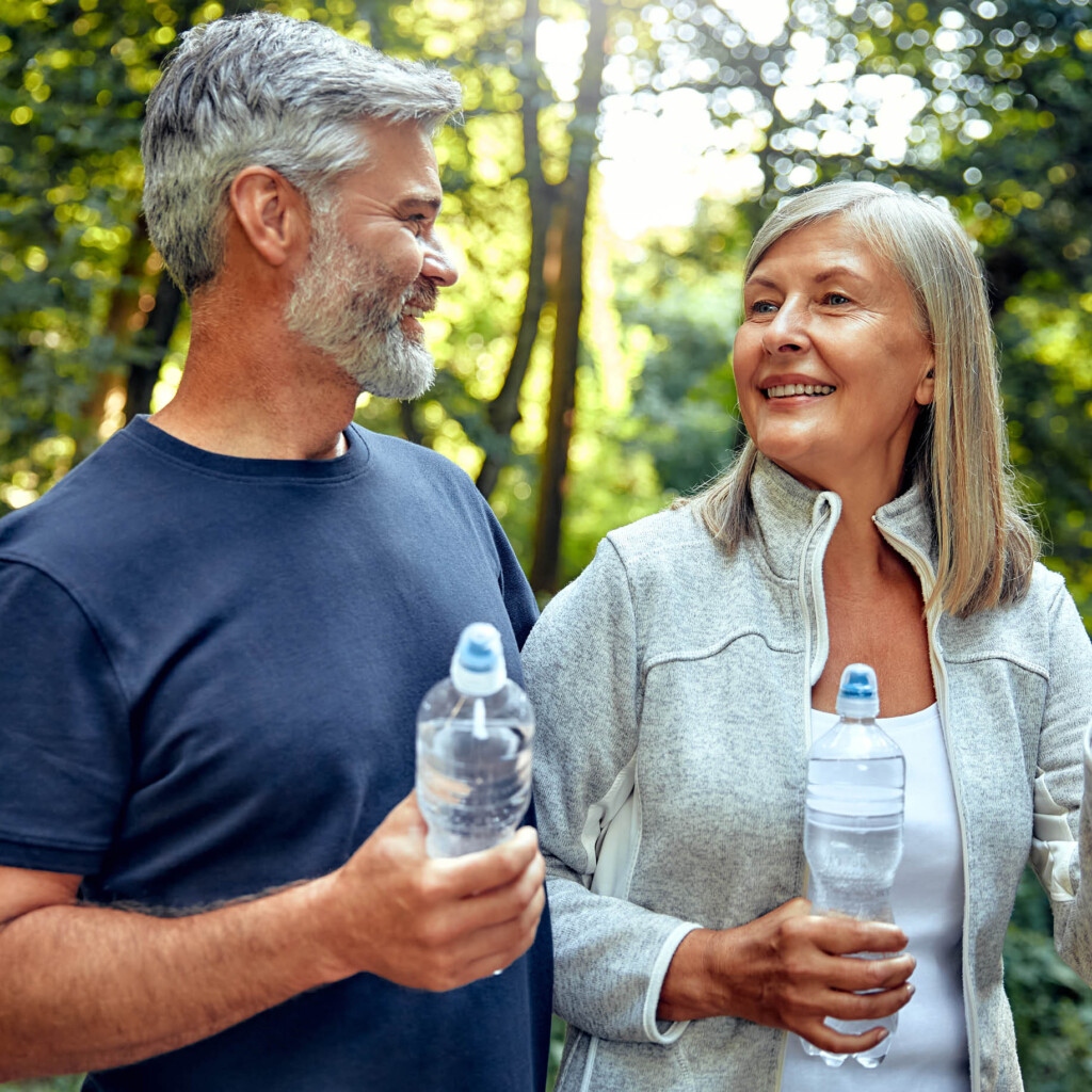 older couple hiking in woods holding water bottles