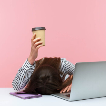 Woman holding coffee cup head on desk at office.