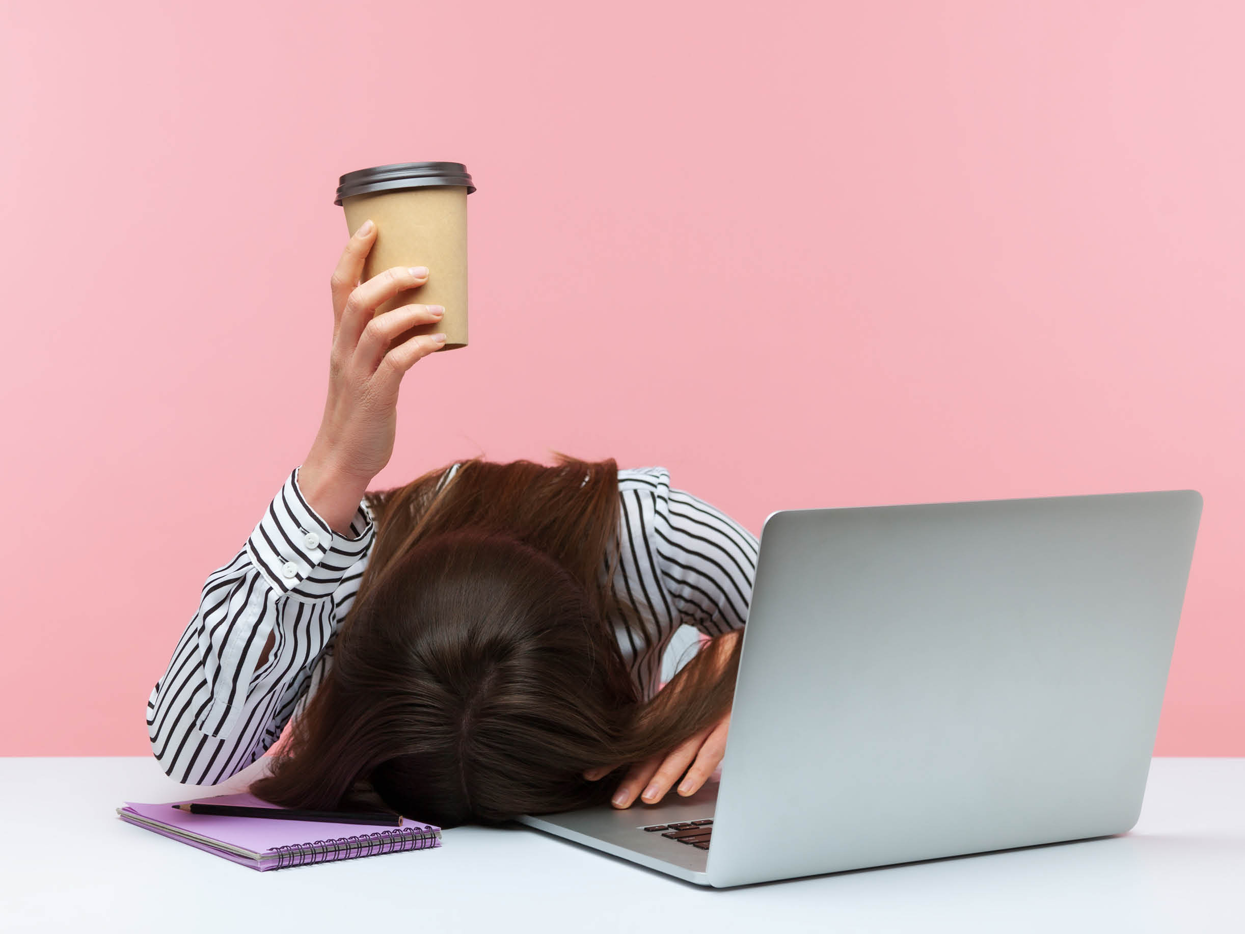Woman holding coffee cup head on desk at office.